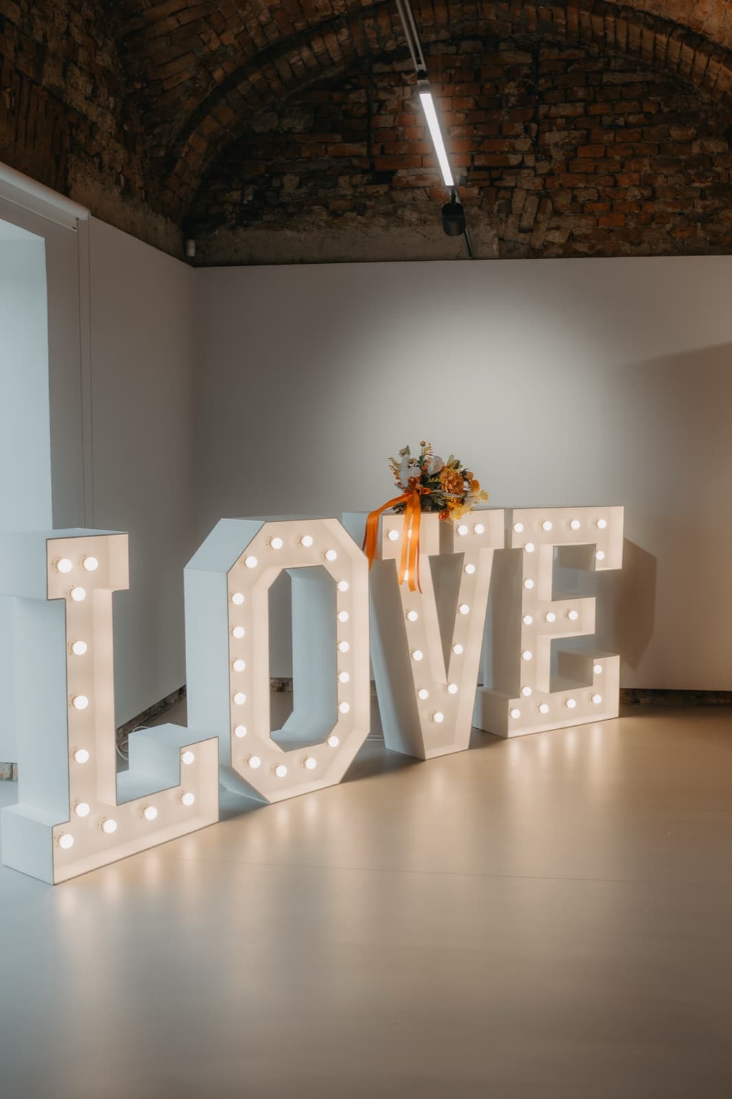 Svítící nápis LOVE v sále s cihlovou klenbou